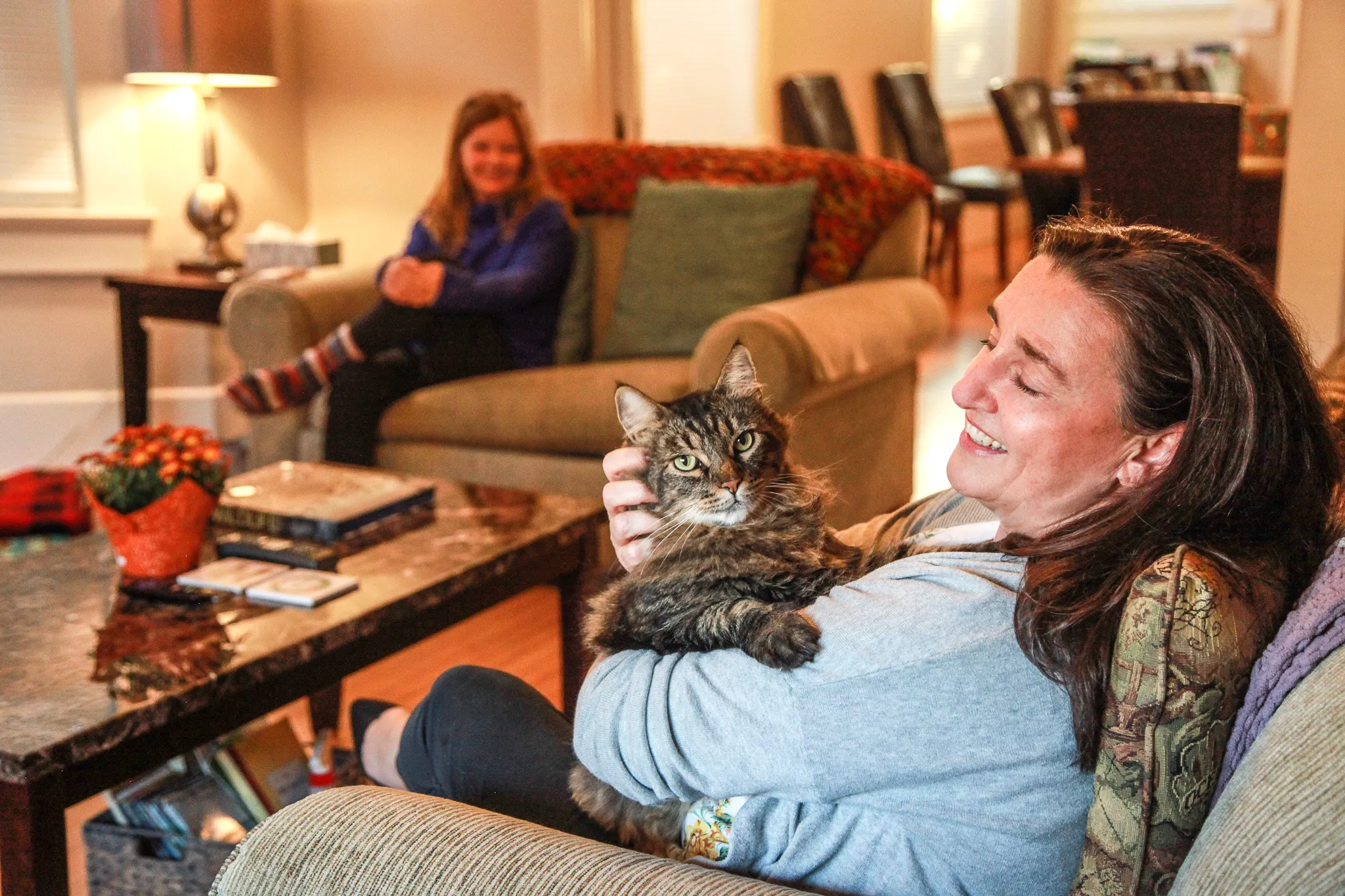 Residents together in the living room — warm lamp light, soft pillows, evening